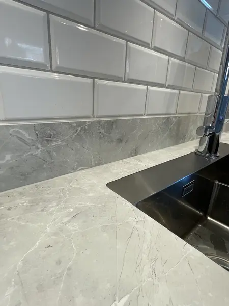 Närbild på rostfri nedsänkt diskho mot ljusgrå bänkskiva och vitt subway-kakel